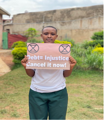 Ein junger Klimaaktivist hält während der Aktion 'Cancel the Debt, Healthe Planet' in Kigali ein Plakat, auf dem "Debt = Injustice — Cancel itnow!" steht.