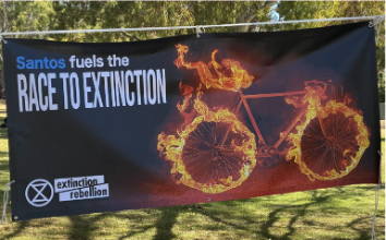 Ein Foto eines Banners, auf dem "Santos fuels the race to extinction"steht, mit einem XR Logo und einem brennendenFahrrad.