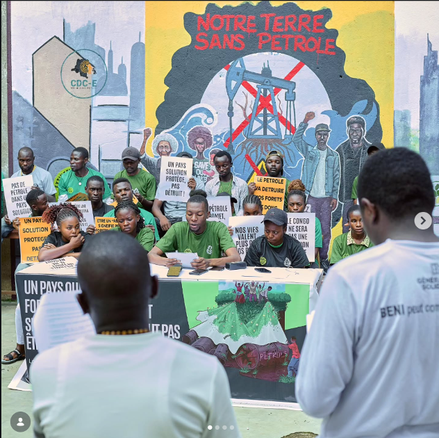 A photo of children and adolescents sitting or standing behind a low table. several hold signs. One reads something aloud.